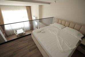 Ein modernes Hotelzimmer mit einem großen Bett, einem Glasbalkon und einer kleinen Schreibtischzeile.