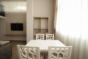 Ein modernes Wohnzimmer mit einem weißen Tisch und Stühlen, einem flachbildfernseher an der Wand und einer eingebauten Bücherwand.