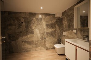 A modern bathroom with a marble wall, a wooden floor, a white toilet, and a white sink with a mirror above it. - Duplex City 02 in Durrës (Durrës)