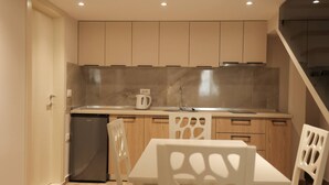 Eine moderne Küche mit Holzausstattung, einem eingebauten Herd und einem Spülbecken. Ein weißer Tisch mit Stühlen und ein kleiner Kühlschrank sind ebenfalls vorhanden.
