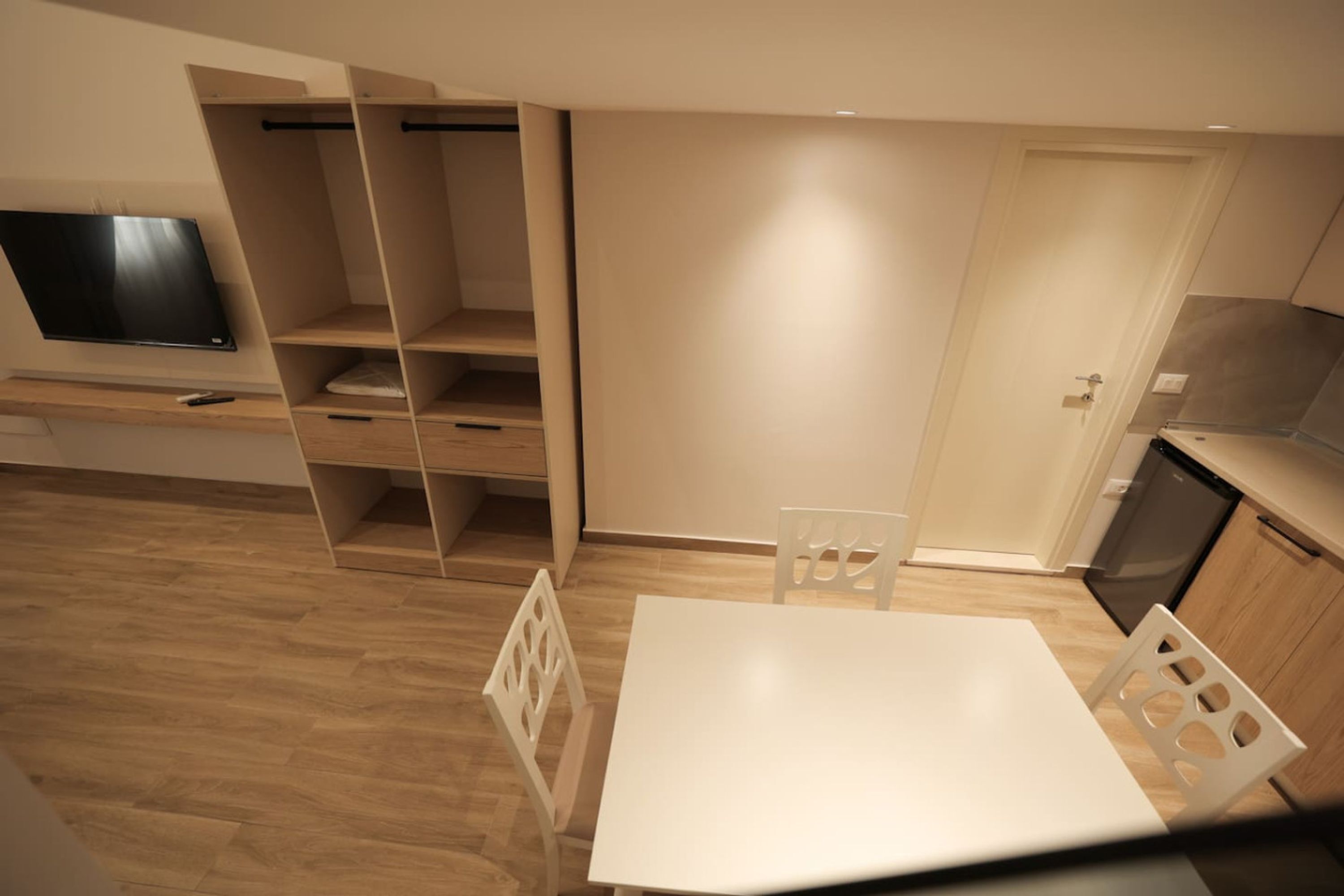 Eine kompakte Küche mit weißem Tisch und Stühlen, Holzschränken und einem integrierten Fernseher.