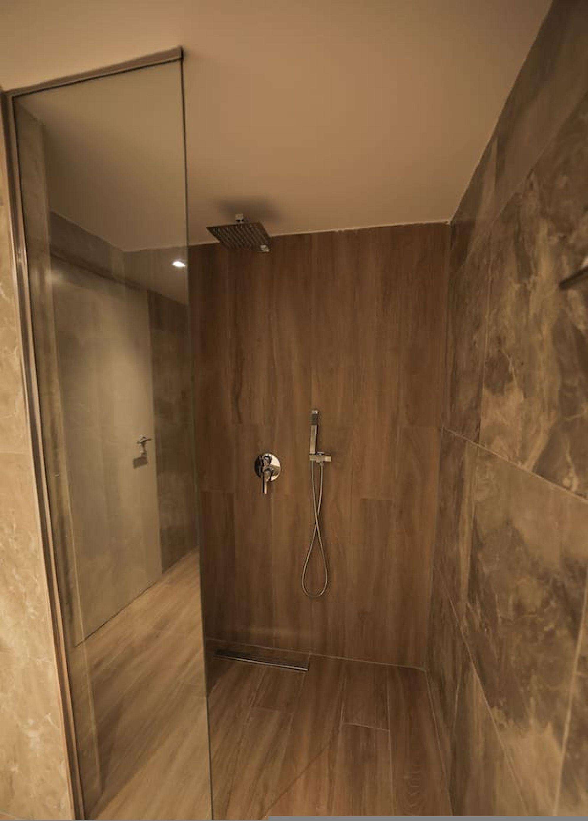 A modern shower room with a glass door, a handheld showerhead, and a wall-mounted faucet.