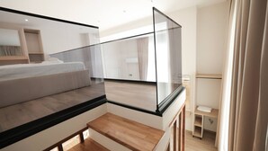 Ein modernes Schlafzimmer mit Glasbalkon, einer hölzernen Bank und Blick auf den angrenzenden Raum.