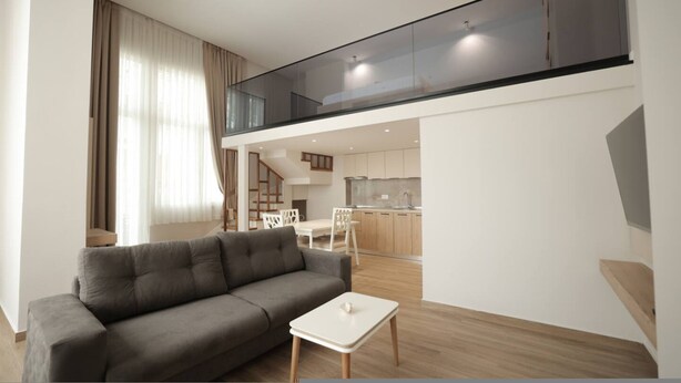 Ein modernes Wohnzimmer mit einem grauen Sofa, einem weißen Couchtisch und einem Glasgeländer mit Blick auf eine Küche und einen Essbereich.
