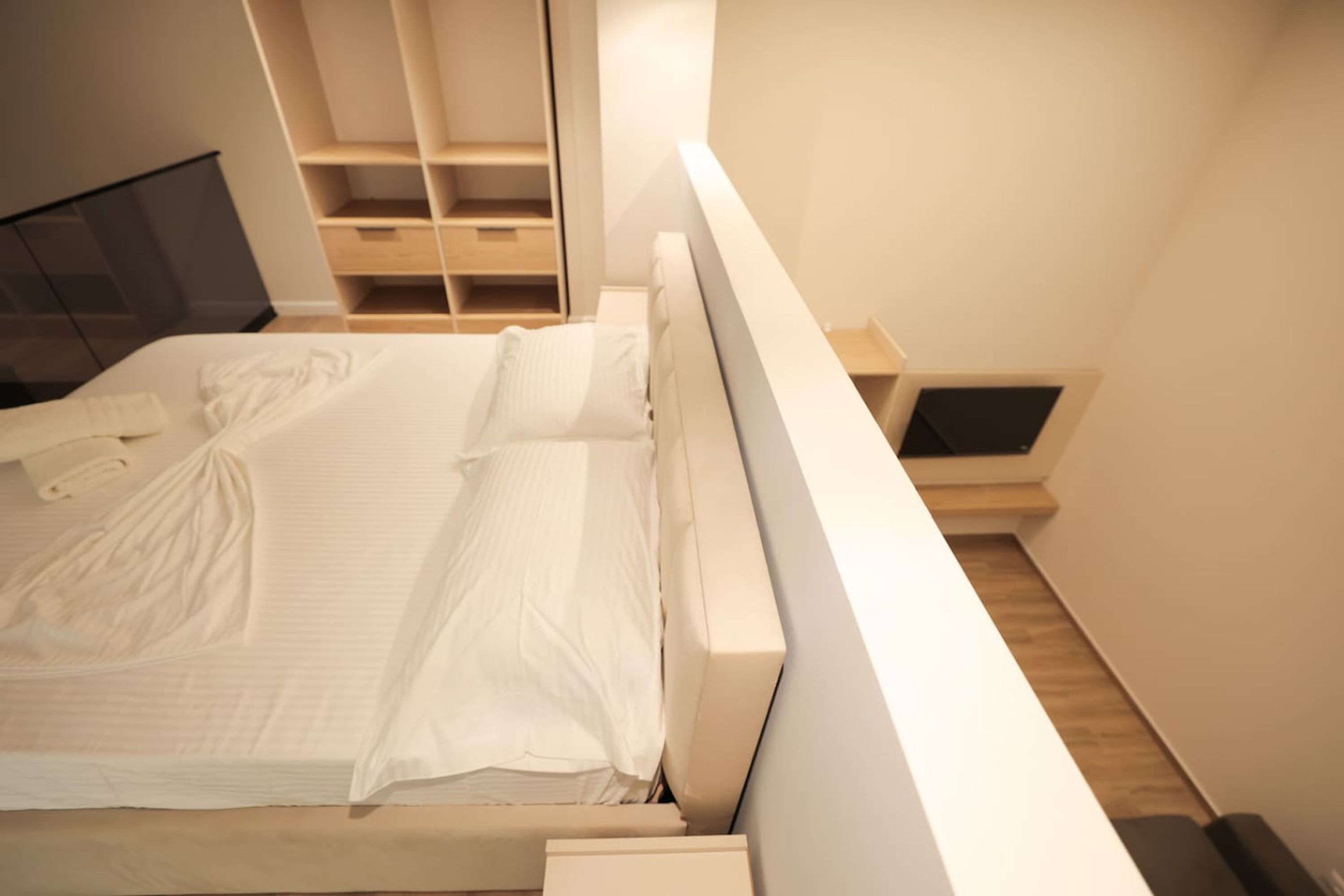 A modern bedroom with a large bed, built-in shelving, and a minimalist design.