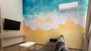 Un salon avec une grande fresque murale, un téléviseur à écran plat, un canapé, une petite table et un climatiseur fixé au plafond.