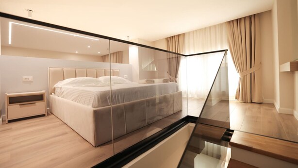 Une chambre moderne avec un grand lit, une table de chevet, une cloison en verre et une vue sur l’extérieur.