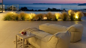 A modern outdoor seating area with a view of the sea, a glass table with fruits, and a minimalist architectural design. - Syvana Exquisite Villas Complex IV (Syvota)