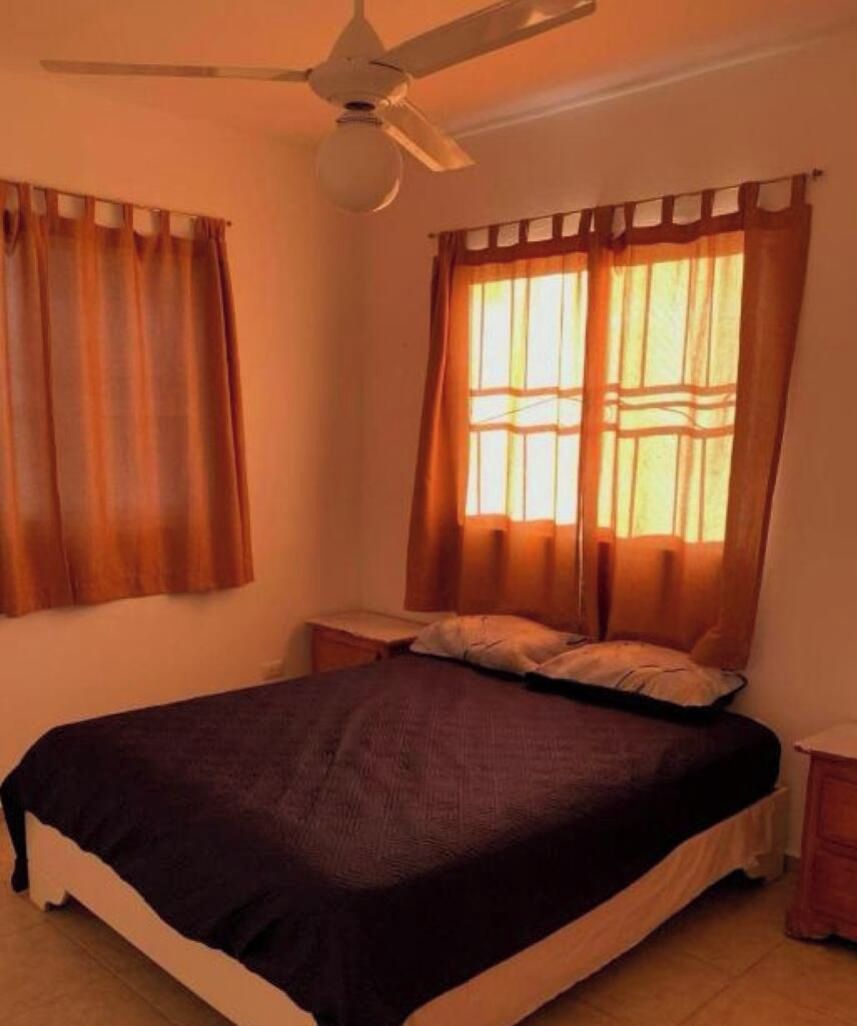 Un dormitorio con cama, cortinas, ventilador de techo y mesita de noche.