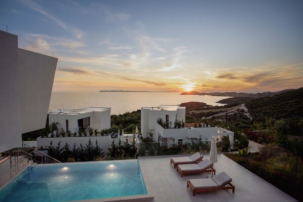 A modern pool area with lounge chairs and a view of the sea at sunset.