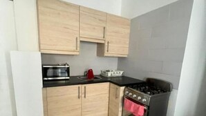 A compact kitchen with light wood cabinets, a black countertop, a stainless steel stove, and a small oven. - apartamento con piscina (Bayahíbe)