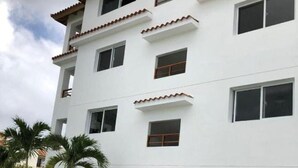 A multi-story building with balconies, a swimming pool, and palm trees. - apartamento con piscina (Bayahíbe)