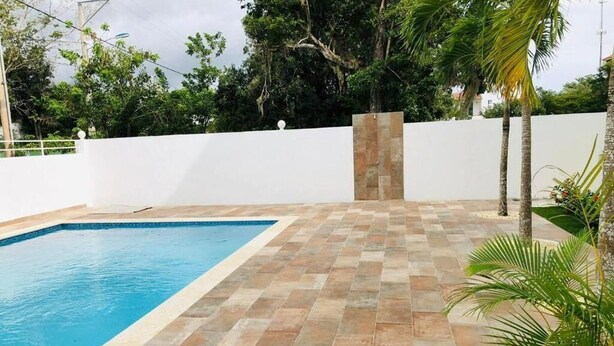 A swimming pool with a tiled deck, surrounded by a white wall and palm trees. - apartamento con piscina (Bayahíbe)