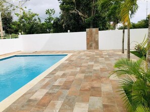 A swimming pool with a tiled deck, surrounded by a white wall and palm trees. - apartamento con piscina (Bayahíbe)