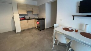 A modern kitchen with light wood cabinets, a gas stove, and a built-in oven. There is a dining area with a white table and chairs. - apartamento con piscina (Bayahíbe)