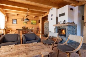 A cozy cabin interior with wooden walls, a stone fireplace, and a dining area with a table and chairs.