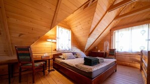 Een slaapkamer in een houten chalet, met een bed, een stoel, een nachtkastje en een raam.