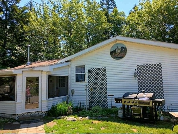Une maison mobile de plain-pied avec un porche, un barbecue et un petit jardin.