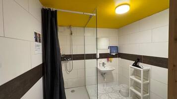 Une petite salle de bain avec une douche, un lavabo et une étagère blanche.