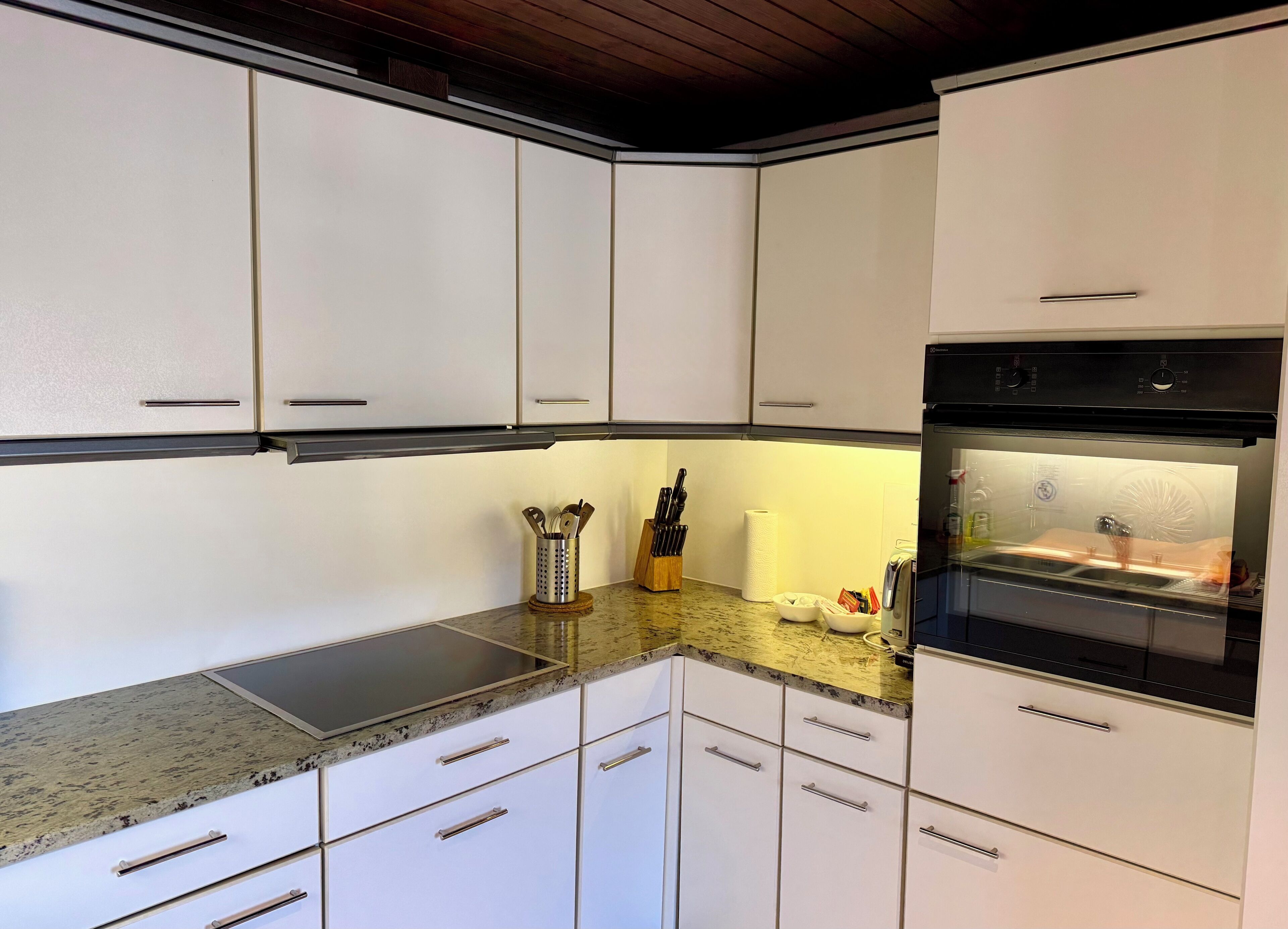 A modern kitchen with white cabinets, a granite countertop, and stainless steel appliances including a dishwasher and oven.