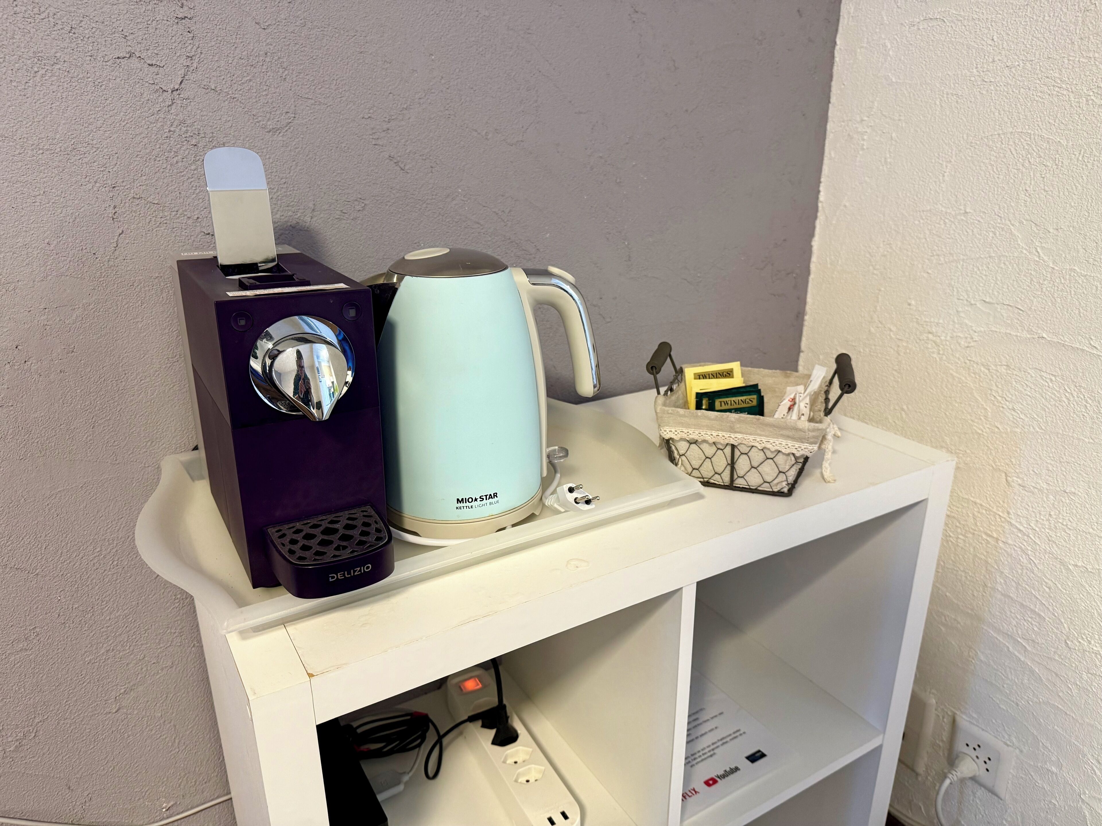 A white shelf with a purple computer tower, a light blue kettle, and a basket containing items.