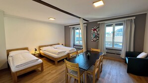 A hotel room with two beds, a dining table with chairs, a black sofa, and large windows with curtains. - DownTown Apartments (Interlaken)