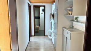 A narrow hallway with a wooden ceiling, leading to a bathroom with a toilet and a shower. A washing machine is visible in the corner. - DownTown Apartments (Interlaken)