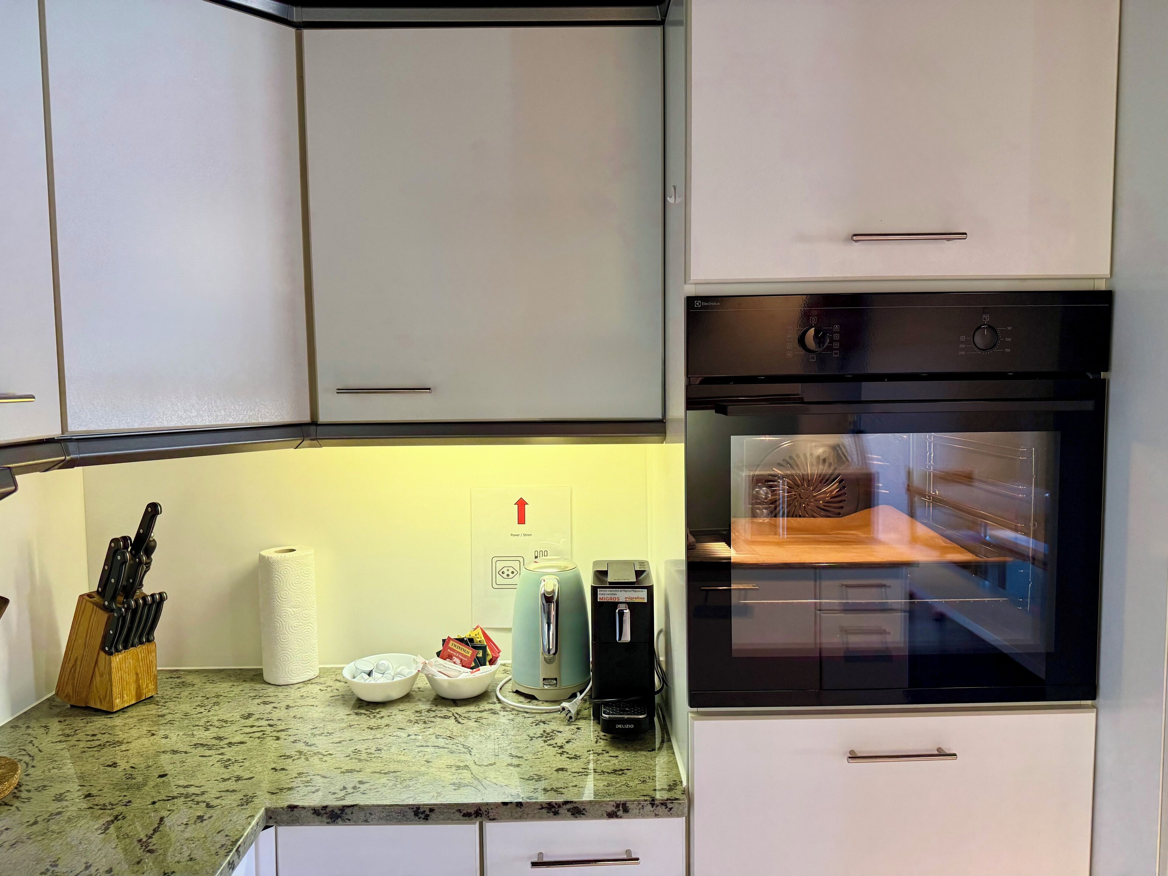 A kitchen with white cabinets, a built-in oven, a coffee maker, and a knife block.