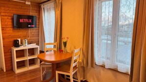 A cozy room with a wooden ceiling, a table with chairs, a TV mounted on the wall, and a window with curtains. - DownTown Apartments (Interlaken)