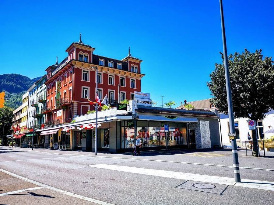 A street view with a red building featuring a 'Café' sign and a storefront with a 'P' parking sign.