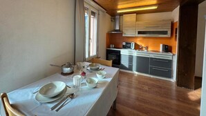 A dining area with a table set for four, a kitchen with modern appliances, and wooden flooring. - DownTown Apartments (Interlaken)