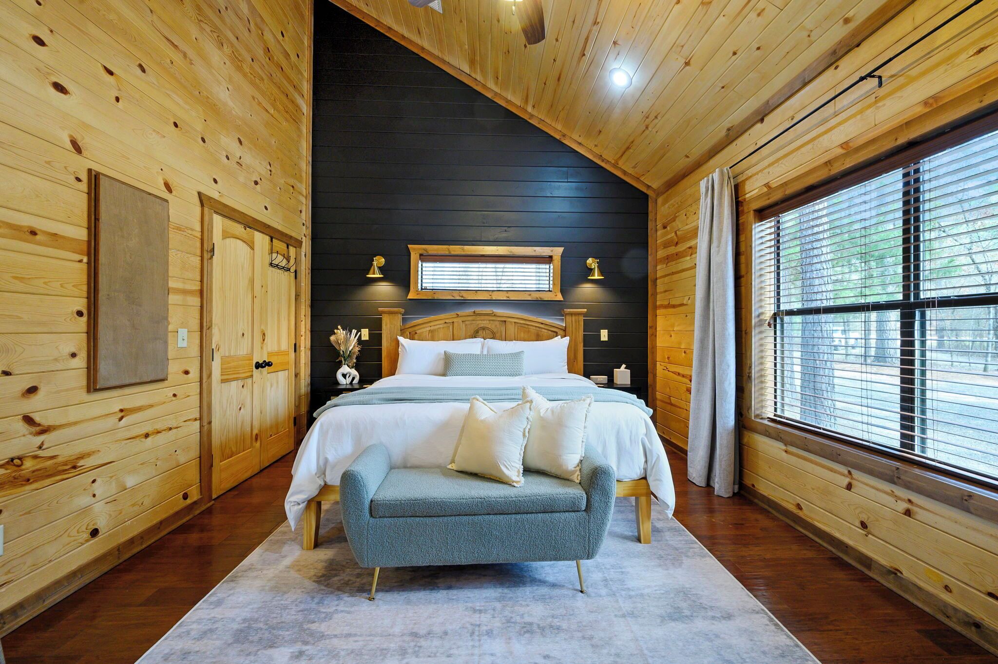 A wooden cabin bedroom with a bed, a bench, a window, and a ceiling light.