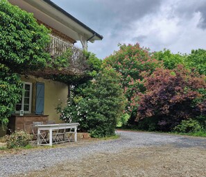A rustic building with a gravel driveway, a wooden bench, and lush greenery.