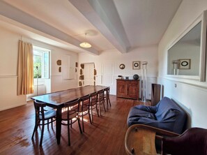 A spacious room with a wooden dining table and chairs, a sofa, and a large window with curtains.