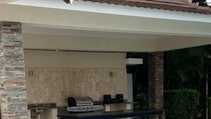 Et udendørs køkkenområde med grill og spisebord, ved siden af en swimmingpool.
