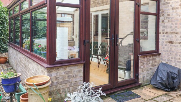 Ein Wintergarten mit Backsteinfassade, großen Glasüren und einem Holzdach.