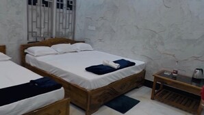 Habitación de hotel con dos camas de madera, suelo de mármol, ventilador de techo y una pequeña mesa de madera con una tetera.