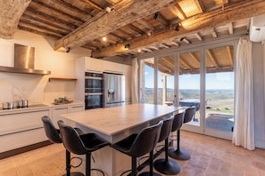 Une cuisine moderne dotée d’un grand îlot central, de tabourets de bar noirs et offrant une vue sur la campagne grâce à de grandes portes coulissantes.