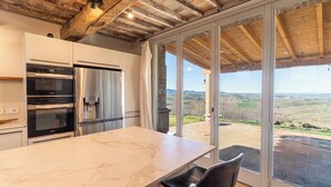 A kitchen with modern appliances, a marble countertop, and a view of the countryside through large sliding glass doors.