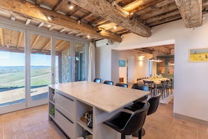Un vaste espace dédié à la salle à manger, avec une grande table en marbre, des chaises noires et une vue sur la campagne grâce à de grandes portes-fenêtres coulissantes.
