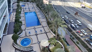 Un edificio alto con piscina y zona de descanso en la azotea, rodeado de palmeras y arquitectura moderna.