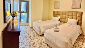 Habitación de hotel con dos camas, un aparador de madera, un florero con flores y un ventanal con vistas a edificios.