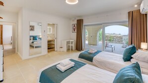 Habitación de hotel con dos camas, baño, escritorio y balcón con vistas.