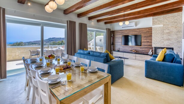 Un salón amplio con una mesa de comedor lista para el desayuno, un sofá azul y un televisor montado en la pared.