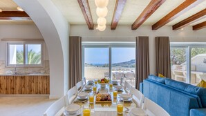 Un comedor con una mesa de madera dispuesta para el desayuno, un sofá azul y grandes ventanales con vistas al paisaje.