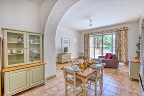 A dining area with a wooden table and chairs, a cabinet with glass doors, and a sofa in the background. - Ta Frenc Apartments - 1 BDR, 1 BTH (L-Għasri)