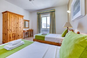 A hotel room with two beds, a wooden wardrobe, a desk, and a window with curtains. - Ta Frenc Apartments - 2 BDR, 1 BTH (L-Għasri)