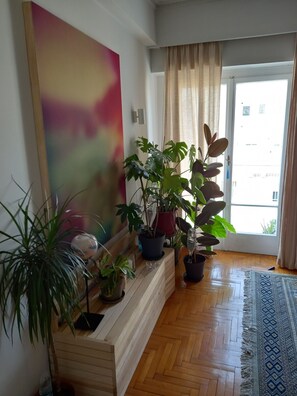 Ein Zimmer mit einer Holzbank, Topfpflanzen, einem großen abstrakten Gemälde und einem gemusterten Teppich.