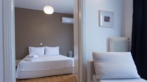 Hotellihuone, jossa on sänky, yöpöytä, lamppu, patteri ja taulu seinällä.