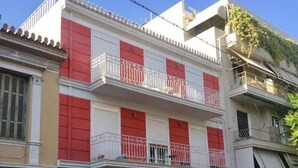 Um edifício de vários andares com varandas, um carro estacionado na frente e uma pequena árvore no jardim.